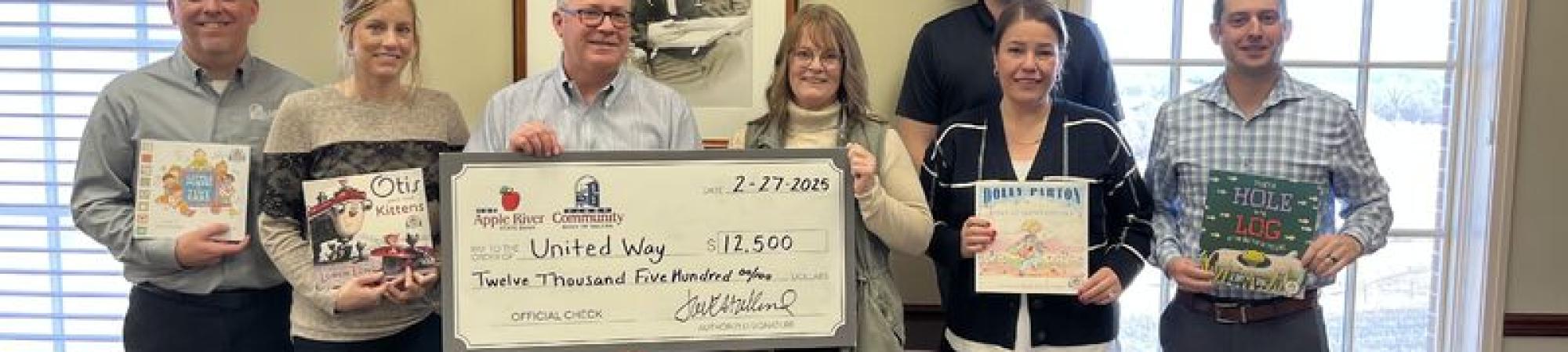 Representatives from Apple River Community Bank present a $12,500 check to United Way while holding children’s books.